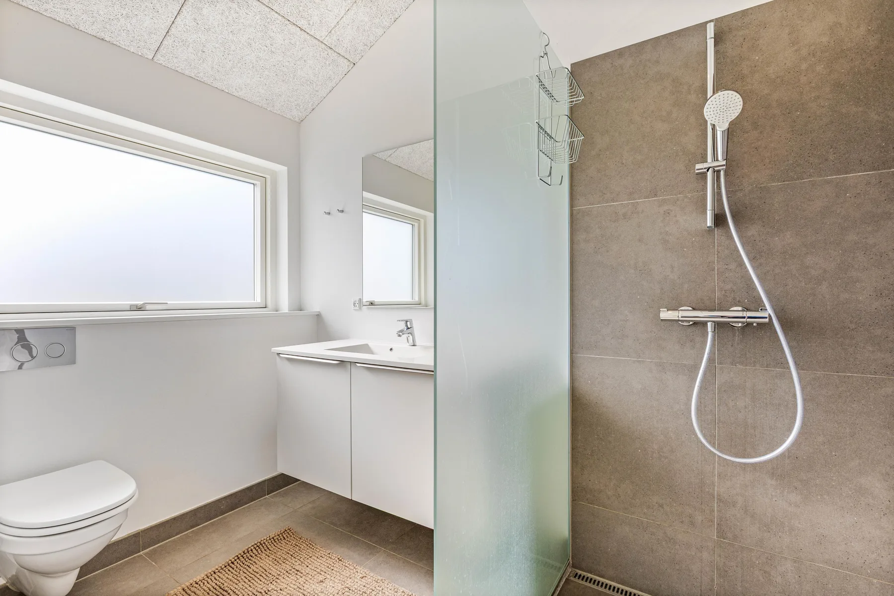 Un baño luminoso con ducha, inodoro y lavabo bajo una ventana.