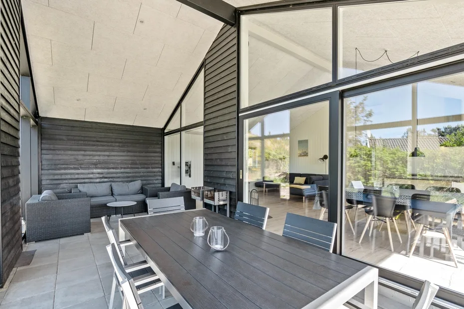 Un patio cubierto con una mesa larga y asientos junto a grandes ventanales.