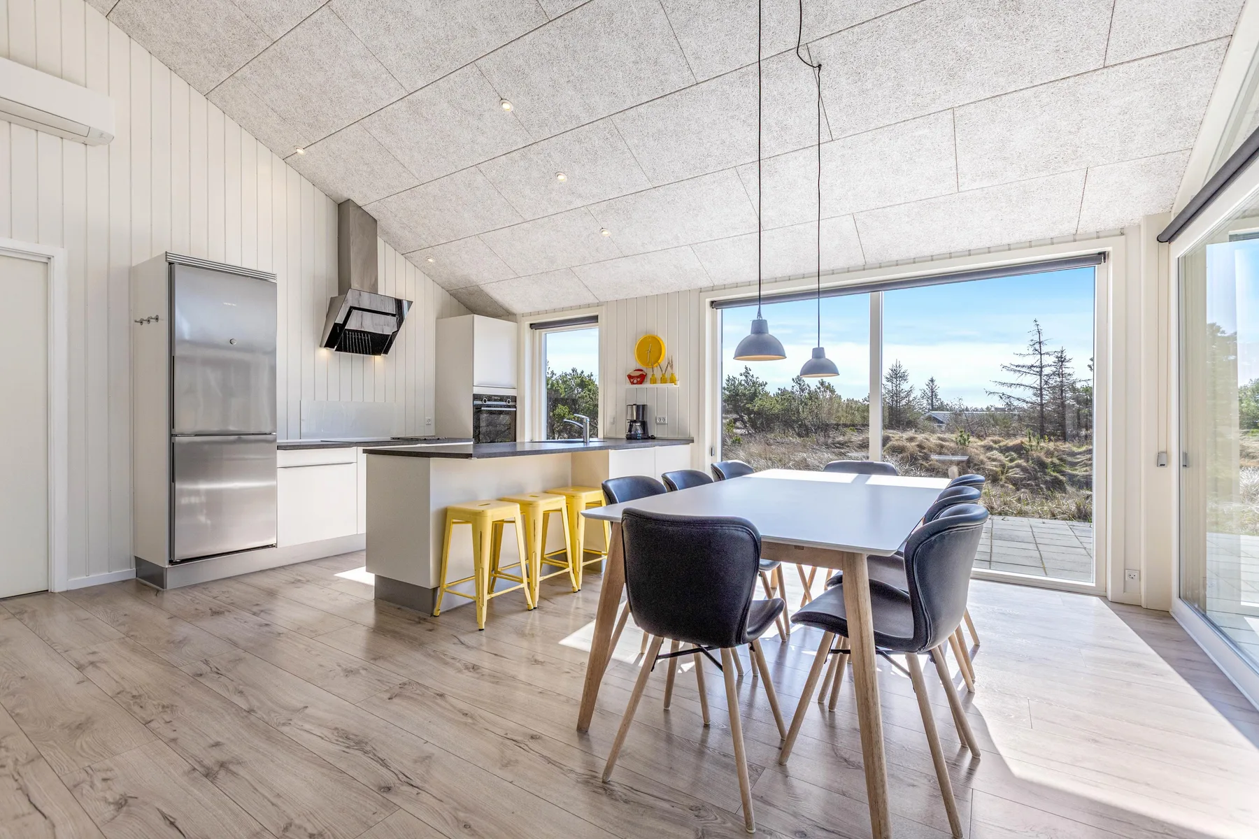 Una cocina luminosa y comedor con una mesa junto a grandes ventanales.