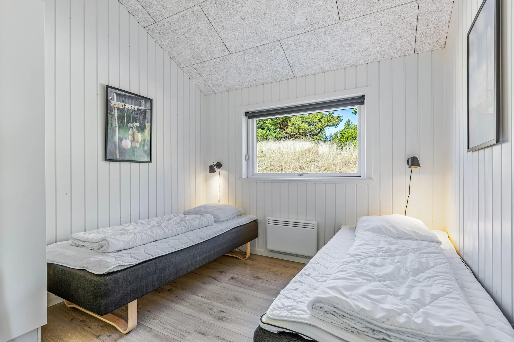 Un dormitorio luminoso con dos camas individuales y una ventana que da a la vegetación.