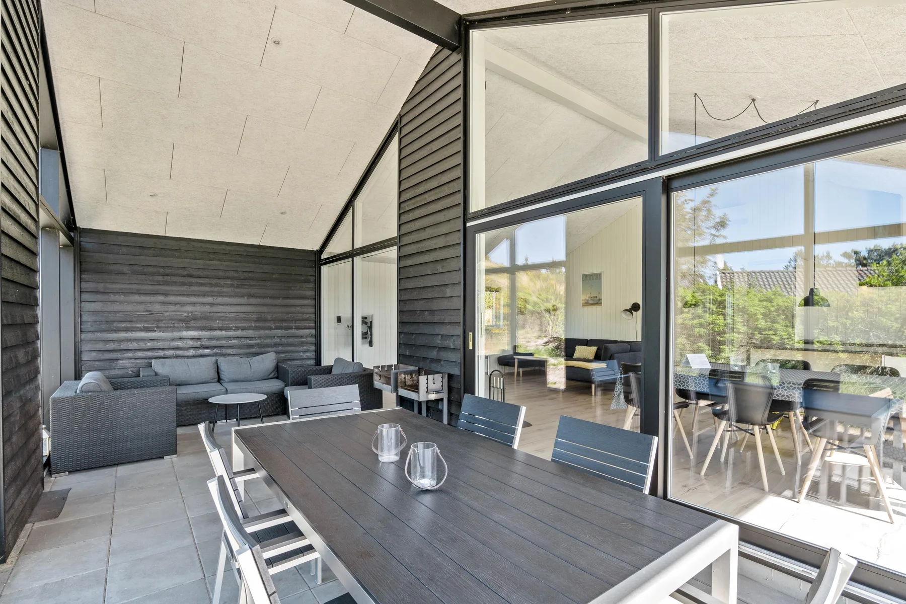 Un patio cubierto con una mesa de comedor y asientos junto a grandes puertas de vidrio.
