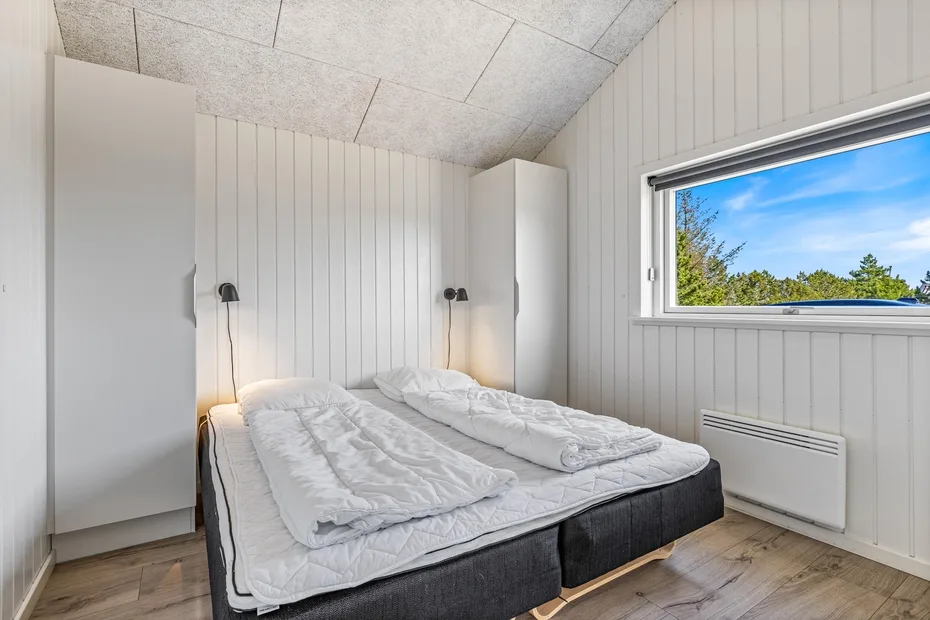 Un dormitorio luminoso con una cama bajo una ventana amplia.