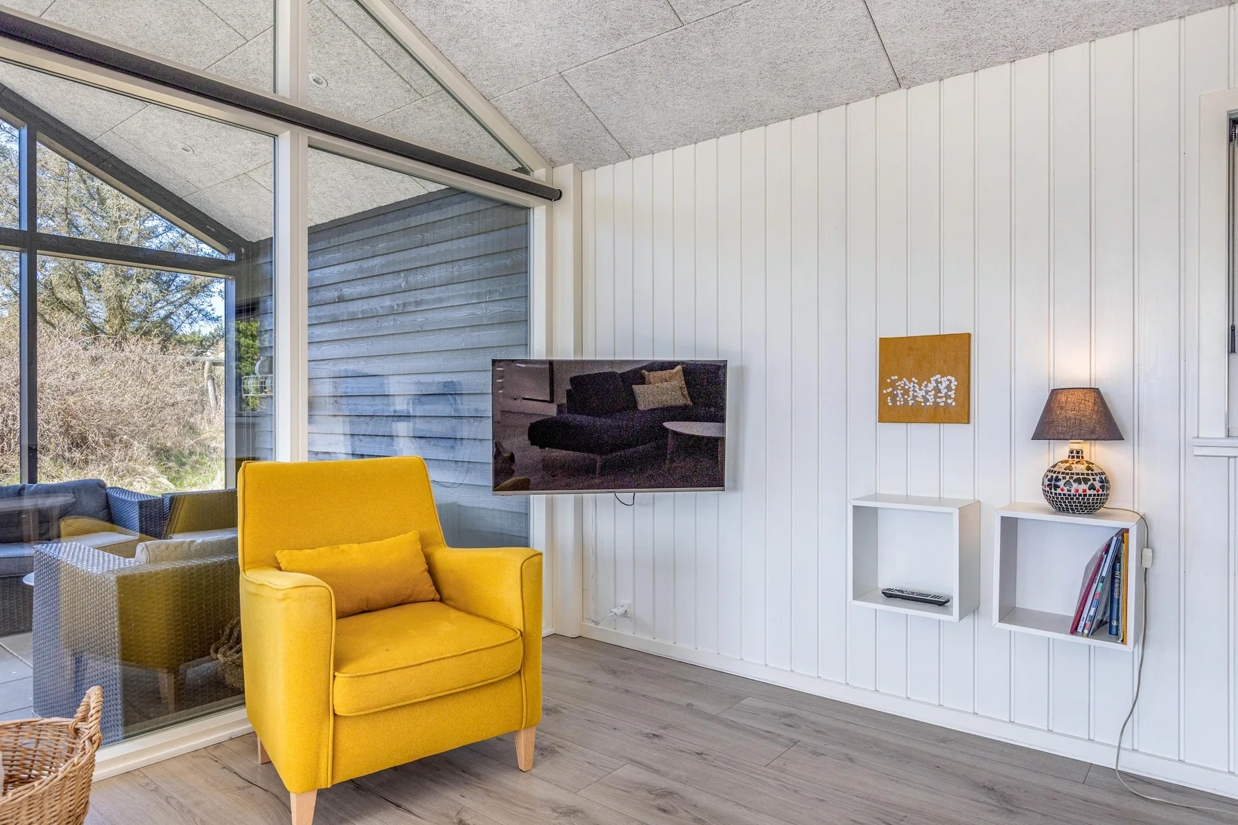 Una sala luminosa con un sillón amarillo junto a grandes ventanas.