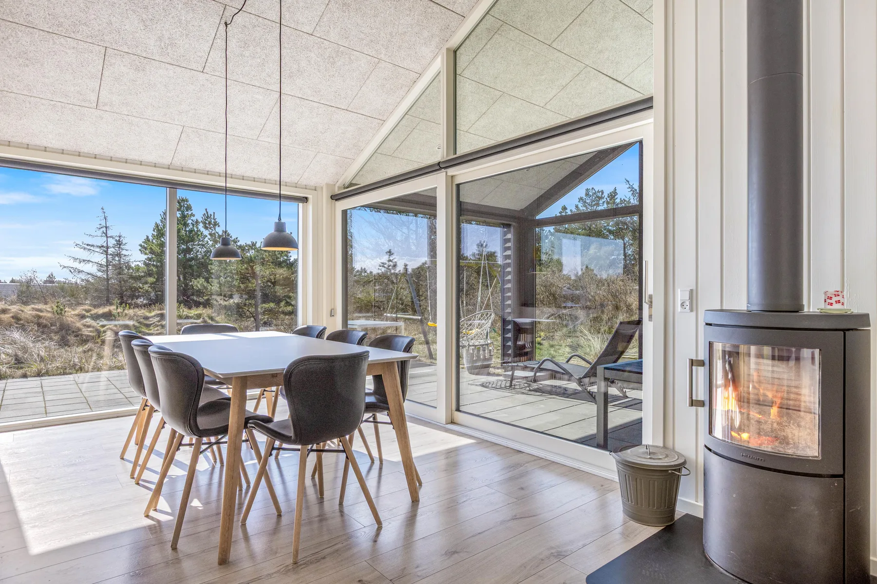 Un comedor luminoso con una mesa junto a grandes ventanales y una chimenea de cristal.