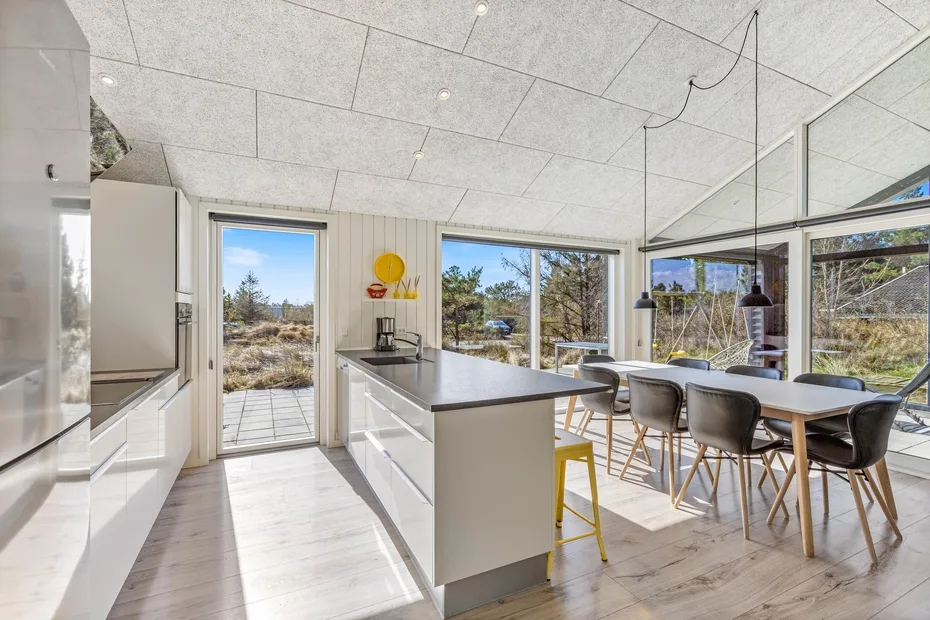 Una cocina y comedor luminosos con grandes ventanas que dan a los árboles.