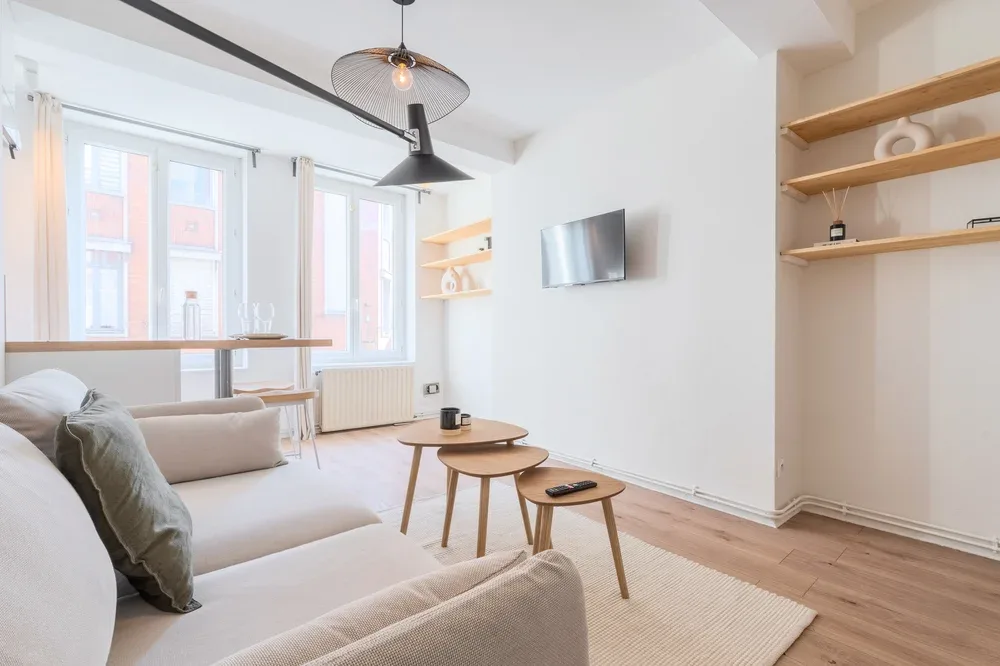 Una sala luminosa con asientos, un televisor en la pared y ventanas grandes.