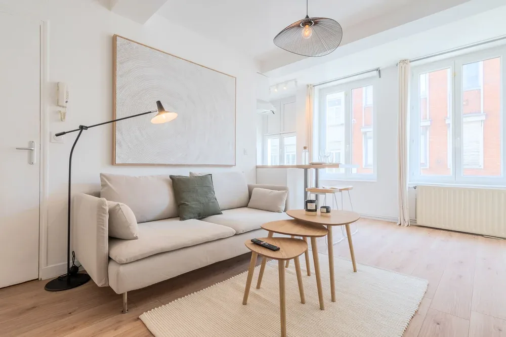 A bright living room with a sofa, nesting tables, and large windows.