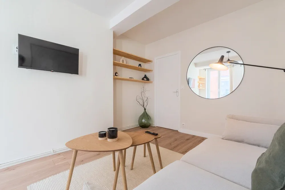 Una sala luminosa con asientos, un televisor en la pared y un espejo redondo.
