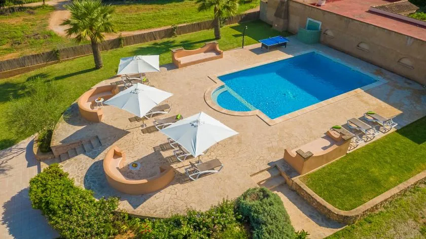 Una piscina y una terraza pavimentada con asientos y sombrillas.
