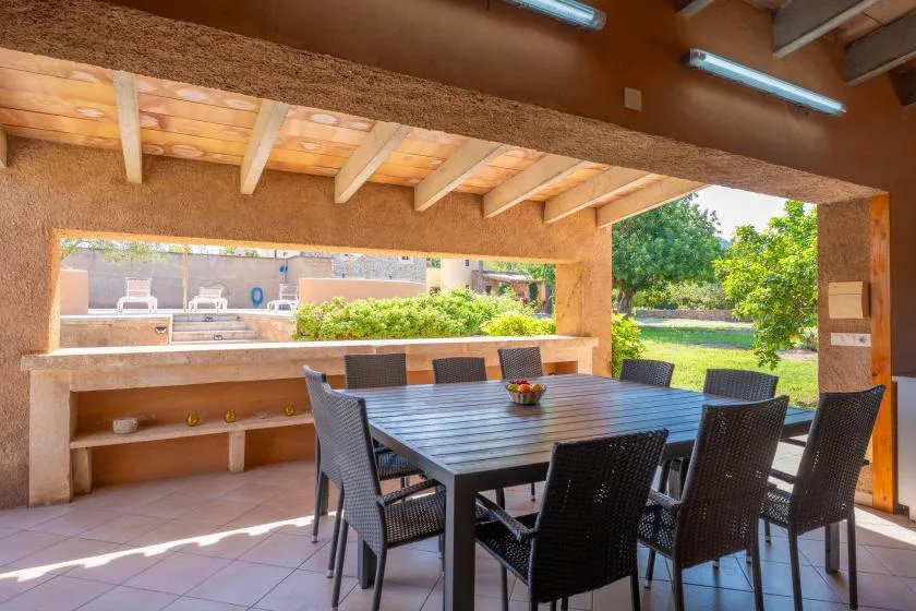 Una zona de comedor exterior cubierta tiene una mesa larga y asientos oscuros.