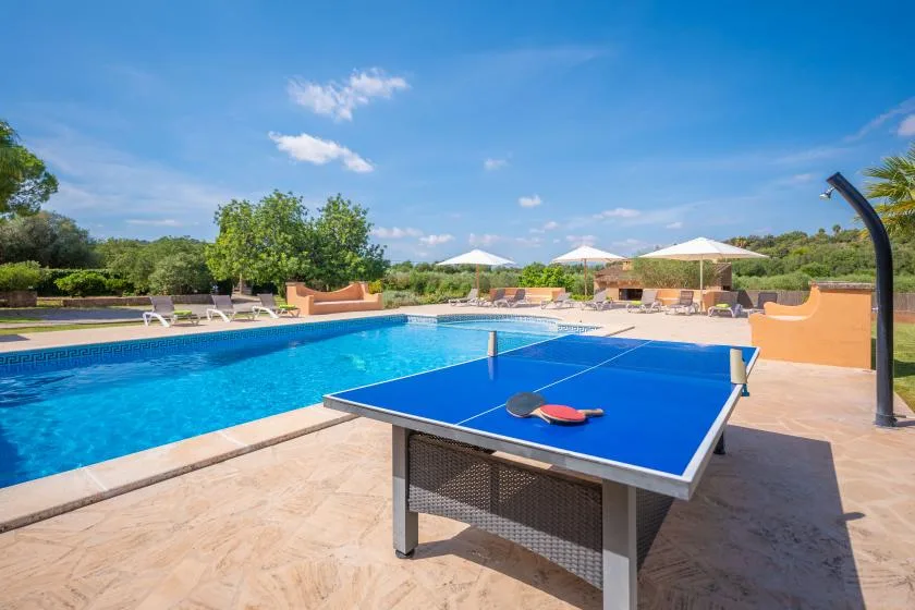 Una piscina al aire libre junto a una mesa de ping-pong azul y asientos.