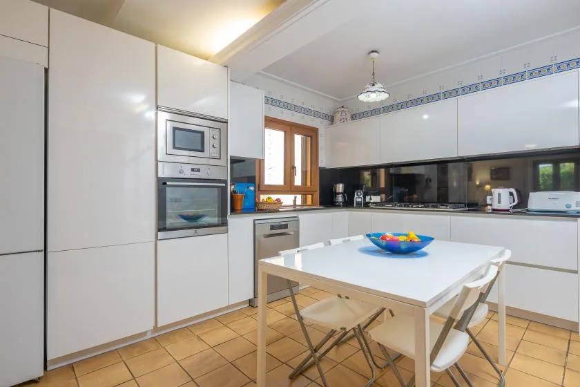 Una cocina luminosa con armarios blancos y una mesa en el centro.