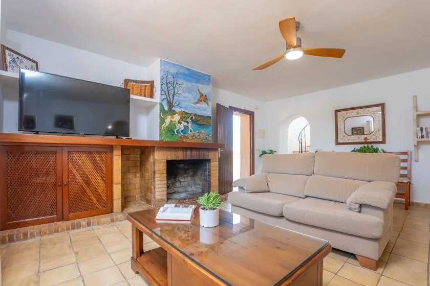 Una sala de estar con sofá, mesa de centro y televisor sobre la chimenea.