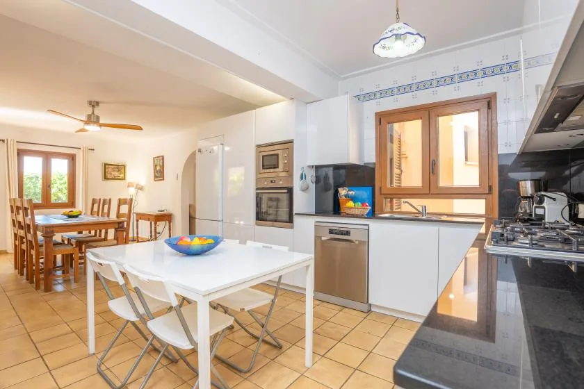 Una cocina y comedor luminosos con una mesa blanca y gabinetes de madera.