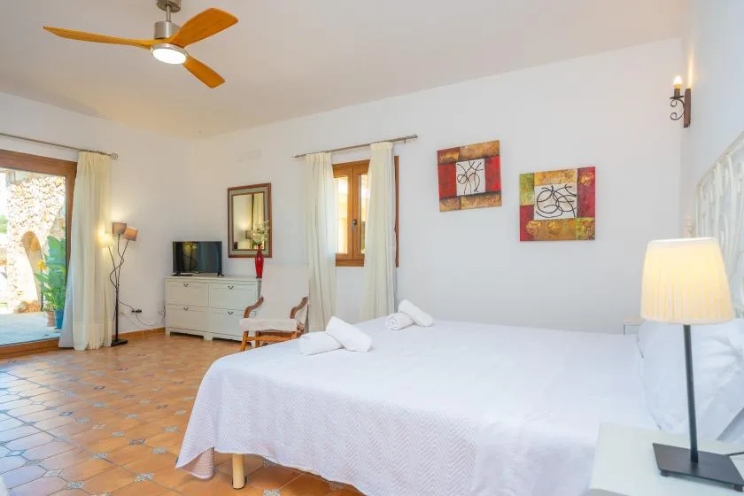 Un dormitorio luminoso con una cama grande, un televisor y un ventilador de techo.