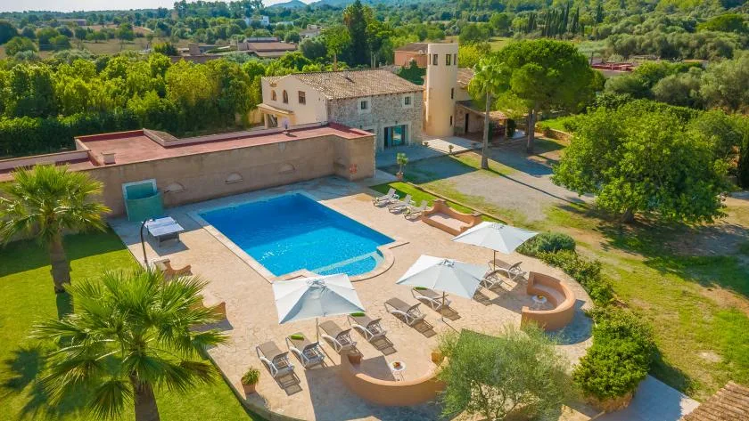 Una piscina al aire libre junto a un edificio de piedra, con asientos en el patio.