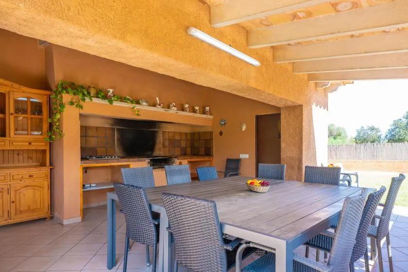 A covered outdoor dining area with a large table and built-in cooking counter.