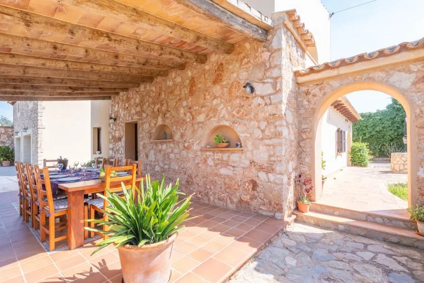Un comedor en un patio de piedra tiene una mesa de madera bajo una terraza cubierta.