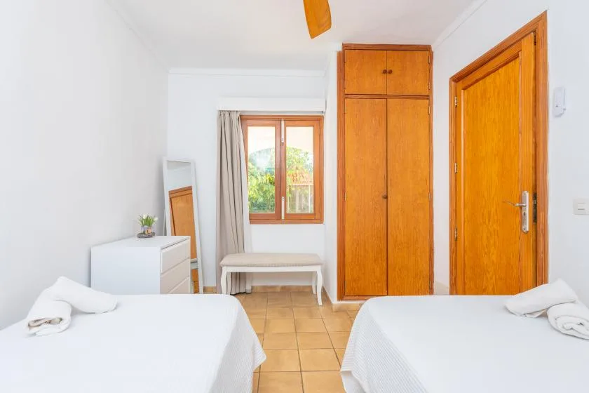 Un dormitorio luminoso con dos camas, una ventana y armarios de madera.