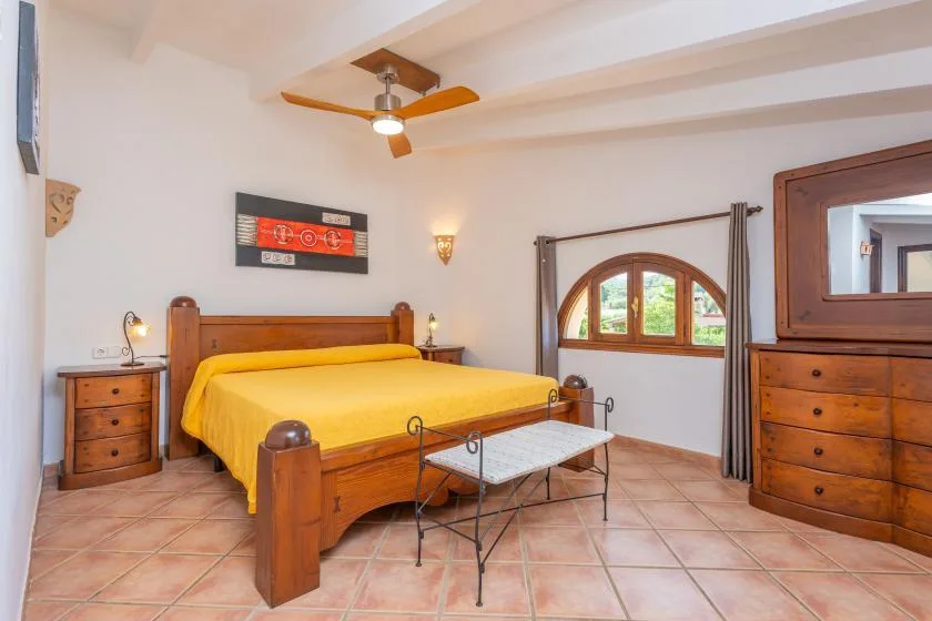 Un dormitorio con una cama de madera cubierta con una colcha amarilla y una mesa pequeña.