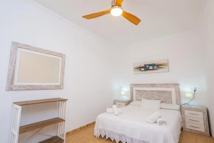 Un dormitorio con una cama, mesitas de noche y un ventilador de techo.