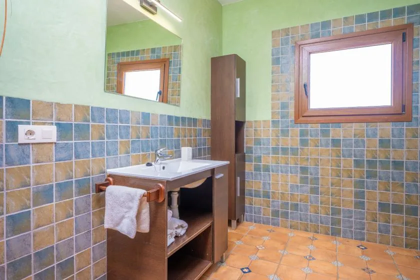 Un baño con azulejos, lavabo con mueble, espejo y ventana.