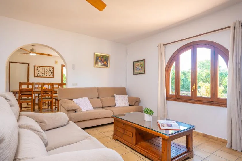 Una sala de estar con asientos tapizados, una mesa de centro de madera y una ventana arqueada.