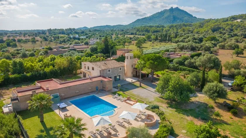 Vista aérea de una piscina junto a edificios, con colinas boscosas a lo lejos.