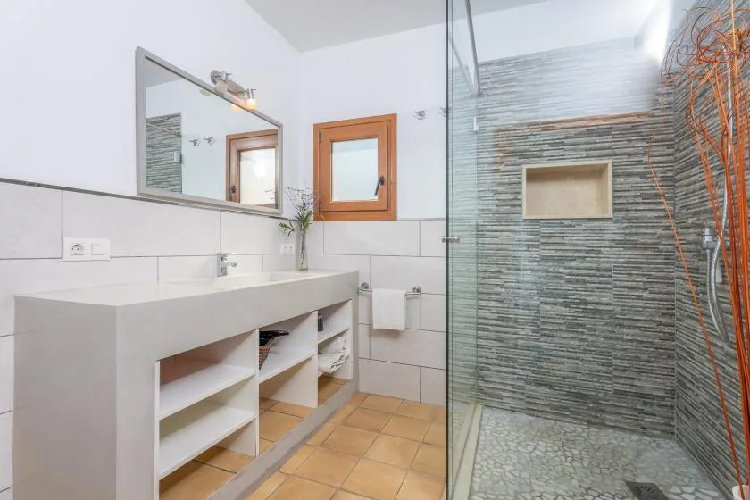 Un baño con una encimera de lavabo larga y una zona de ducha con azulejos.