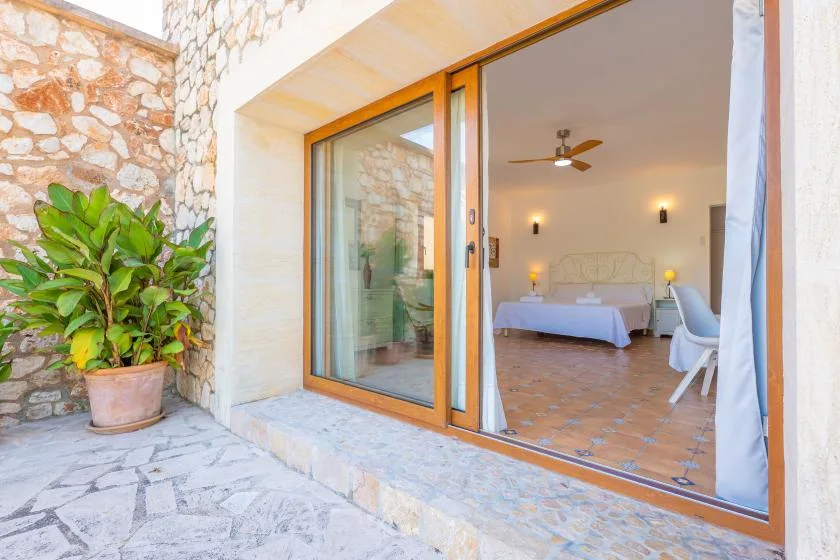 Se ve un dormitorio con una cama a través de puertas corredizas de vidrio abiertas, junto a un patio de piedra.