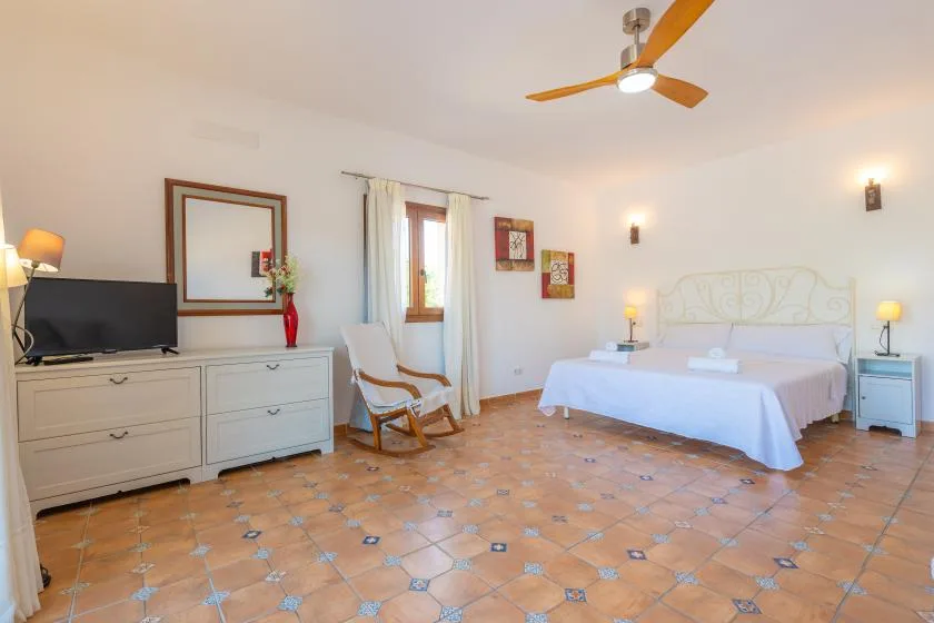 Un dormitorio luminoso con una cama, una cómoda y un sillón.