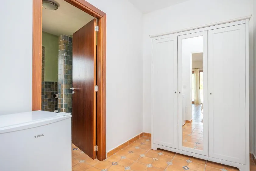 Dormitorio con un armario blanco y una puerta abierta a un baño con azulejos.