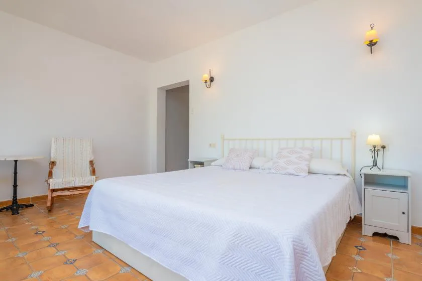 Un dormitorio con una cama grande, mesitas de noche y baldosas de color terracota.