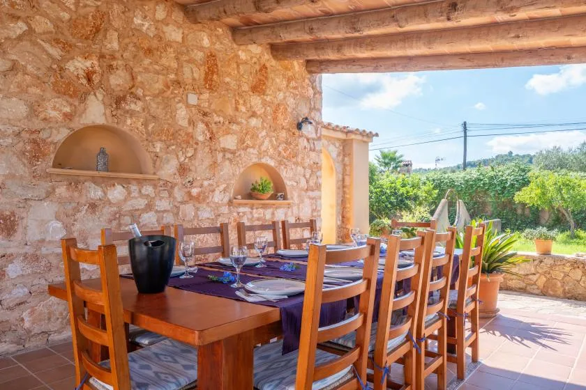 A rustic outdoor dining area with a long wooden table beside a stone wall.