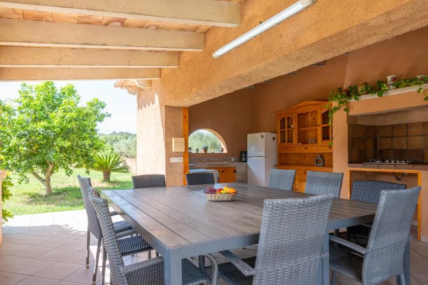 A covered outdoor dining area with a large table and a kitchen.