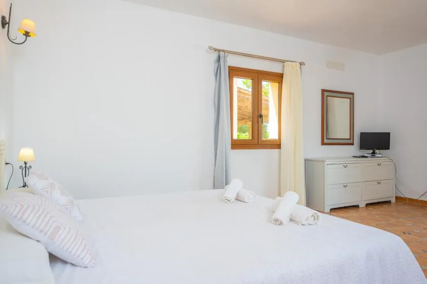 Un dormitorio con una cama tendida, una ventana con cortinas y una cómoda.