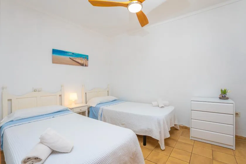 Un dormitorio con dos camas, ropa de cama blanca y un ventilador de techo.