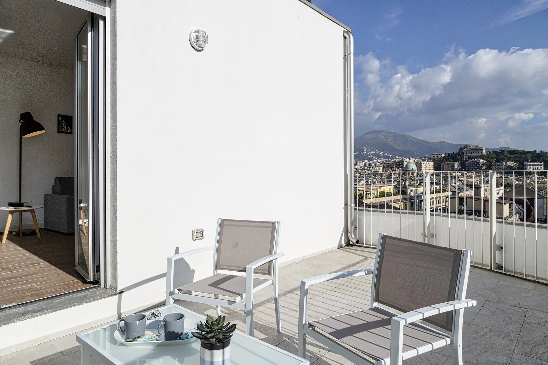 A sunny terrace with seating and a view of the mountains and surrounding buildings.