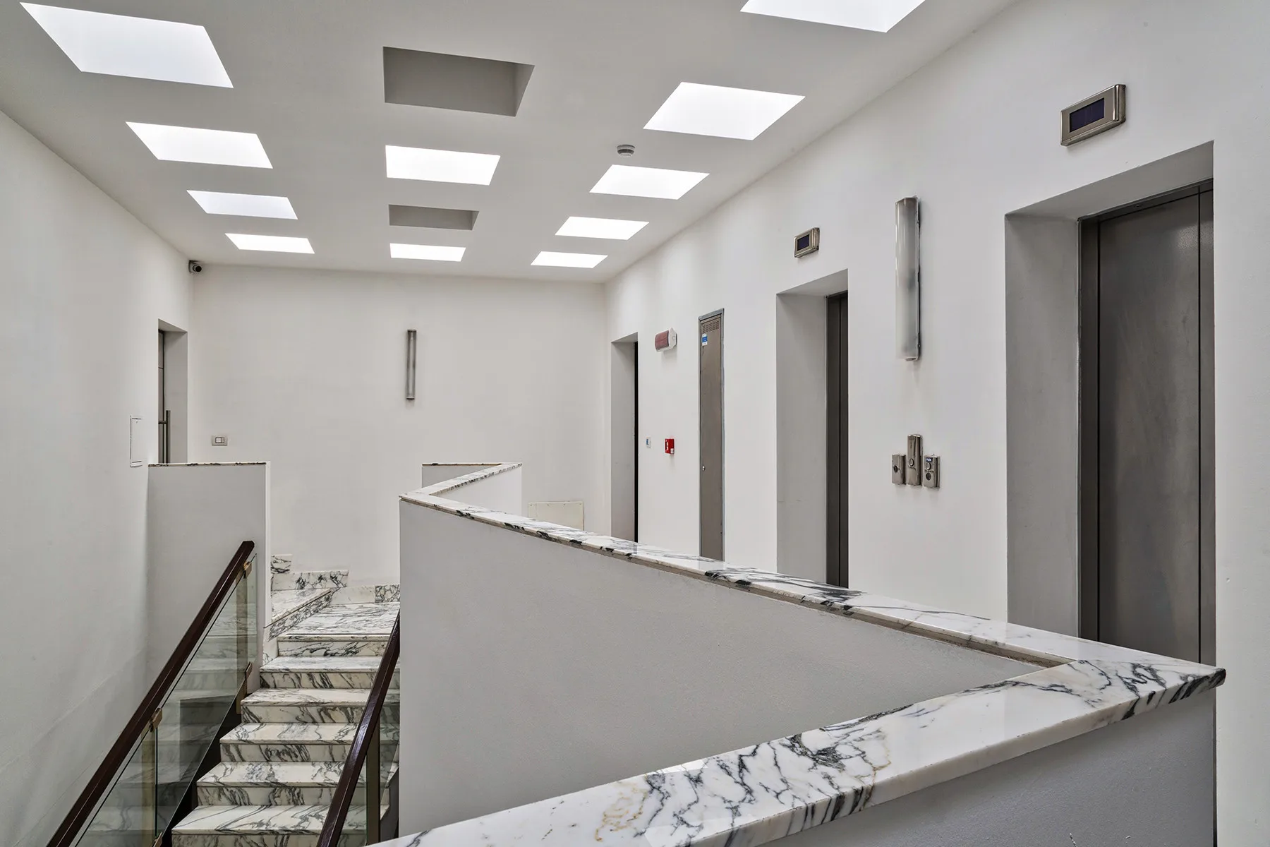 A bright interior hallway with elevator doors and a stair railing.