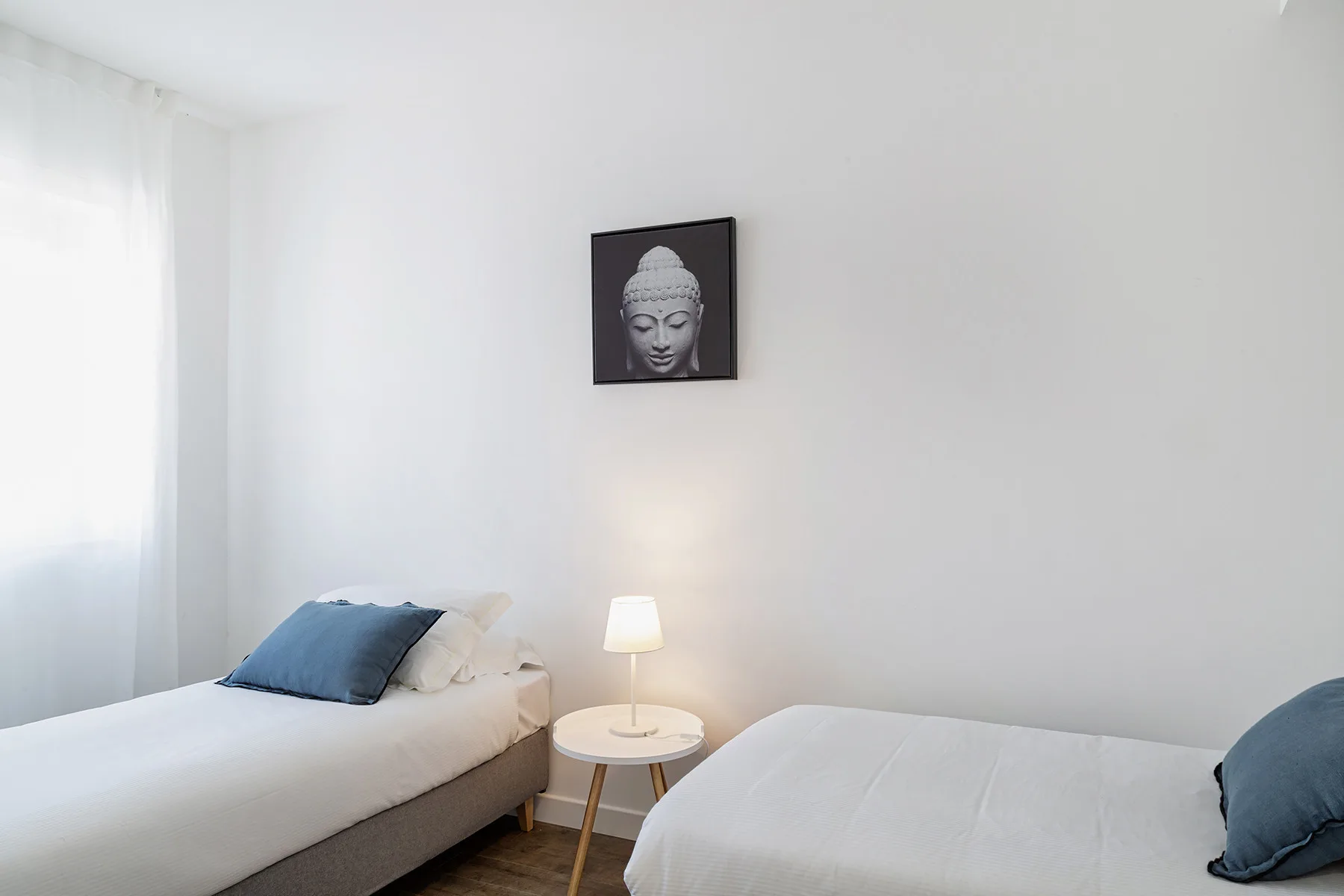 A bright bedroom with two beds and a framed portrait on the wall.
