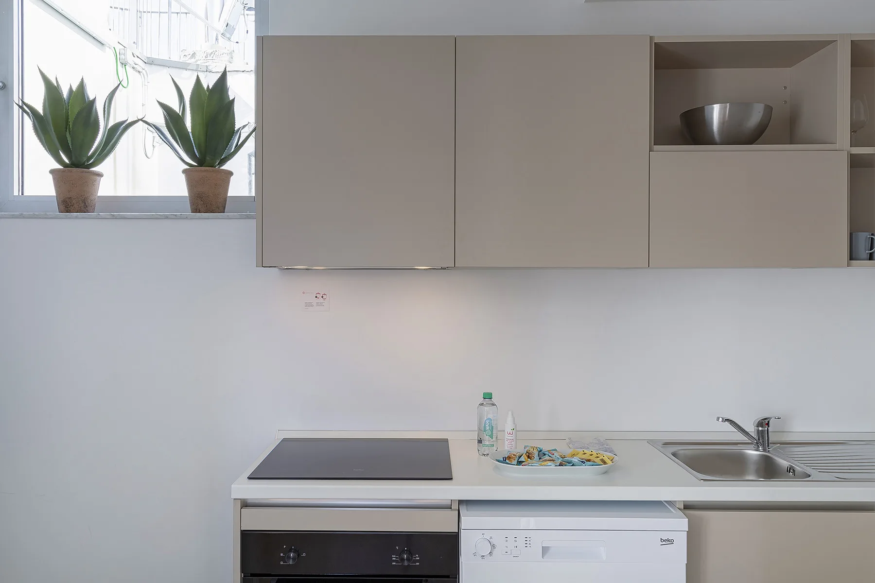 A compact kitchen with a cooktop, sink, and pale cabinets.