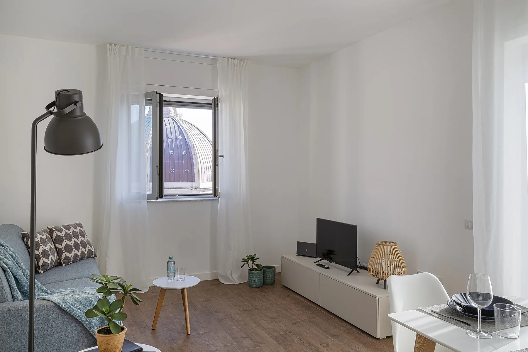 A bright living room with seating, a television, and a small dining area.