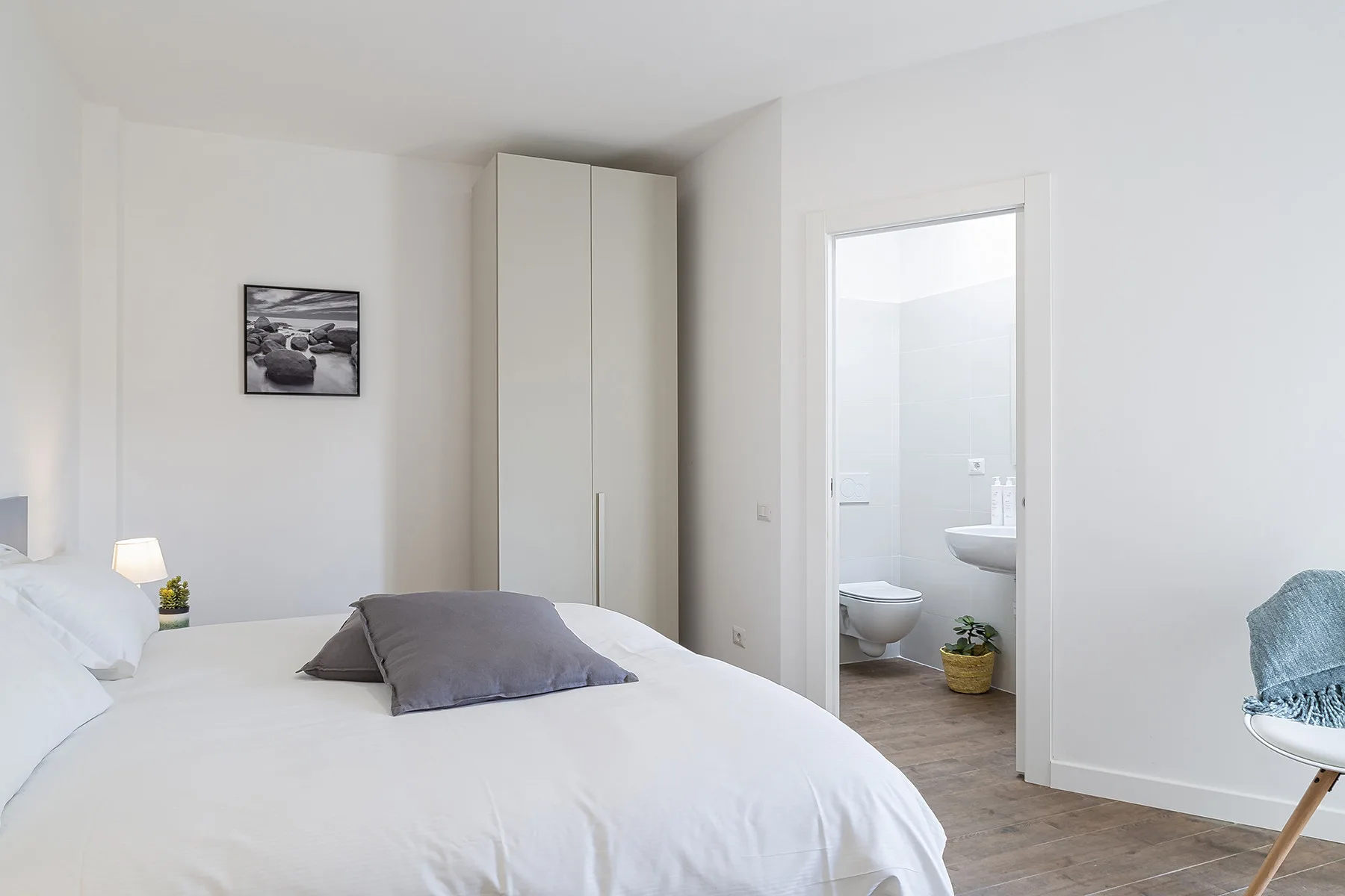 A bright bedroom with a neatly made bed and an open bathroom doorway.
