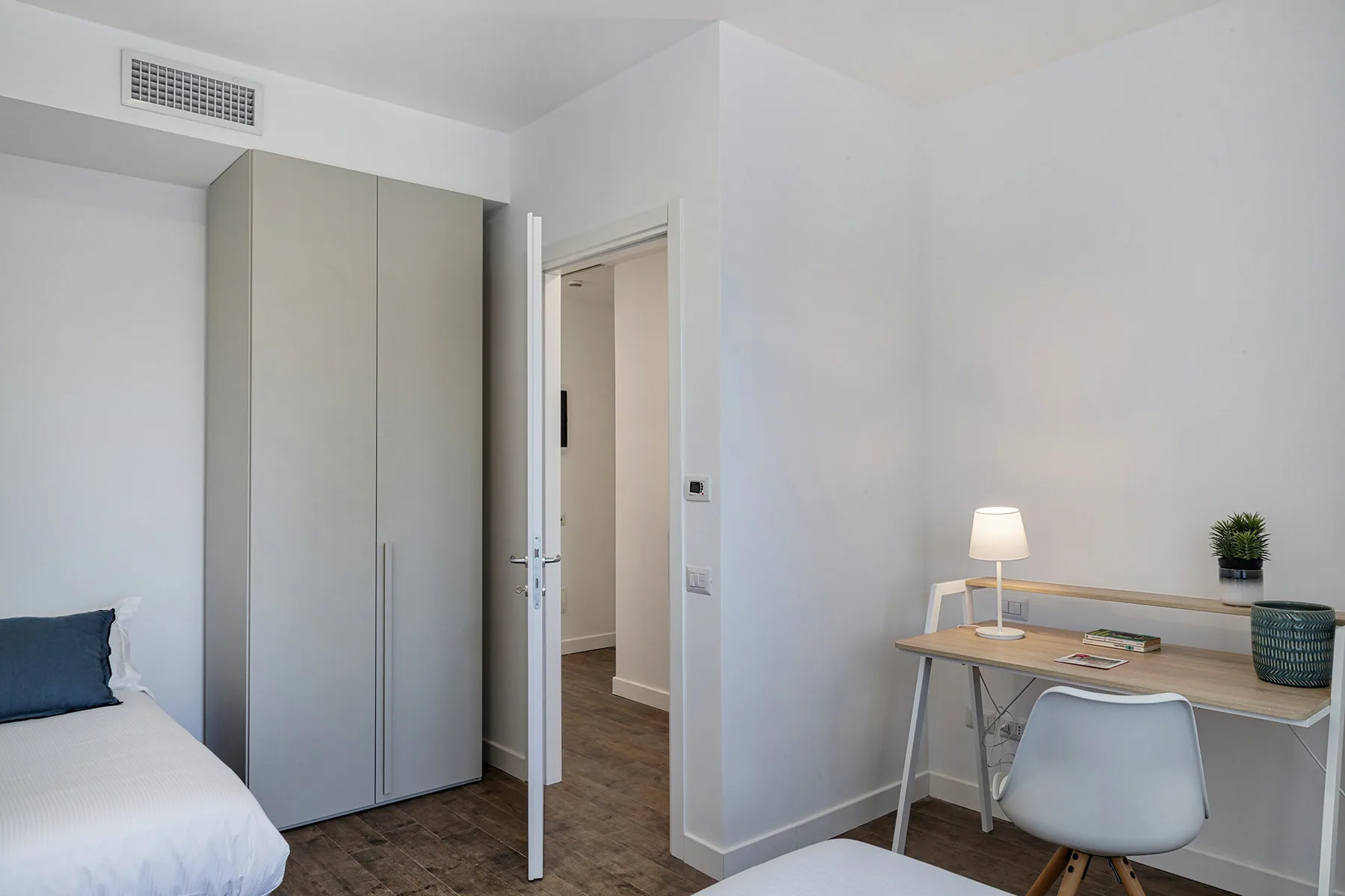 A bright bedroom with a desk, chair, and wardrobe.