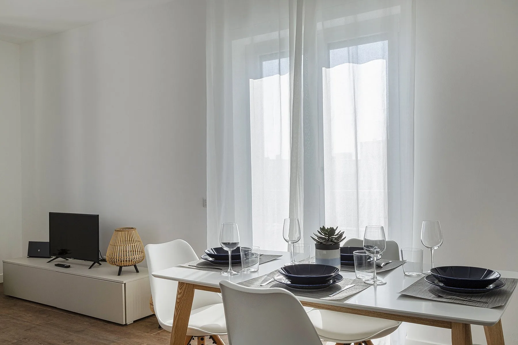 Dining area with a set table beside tall windows.