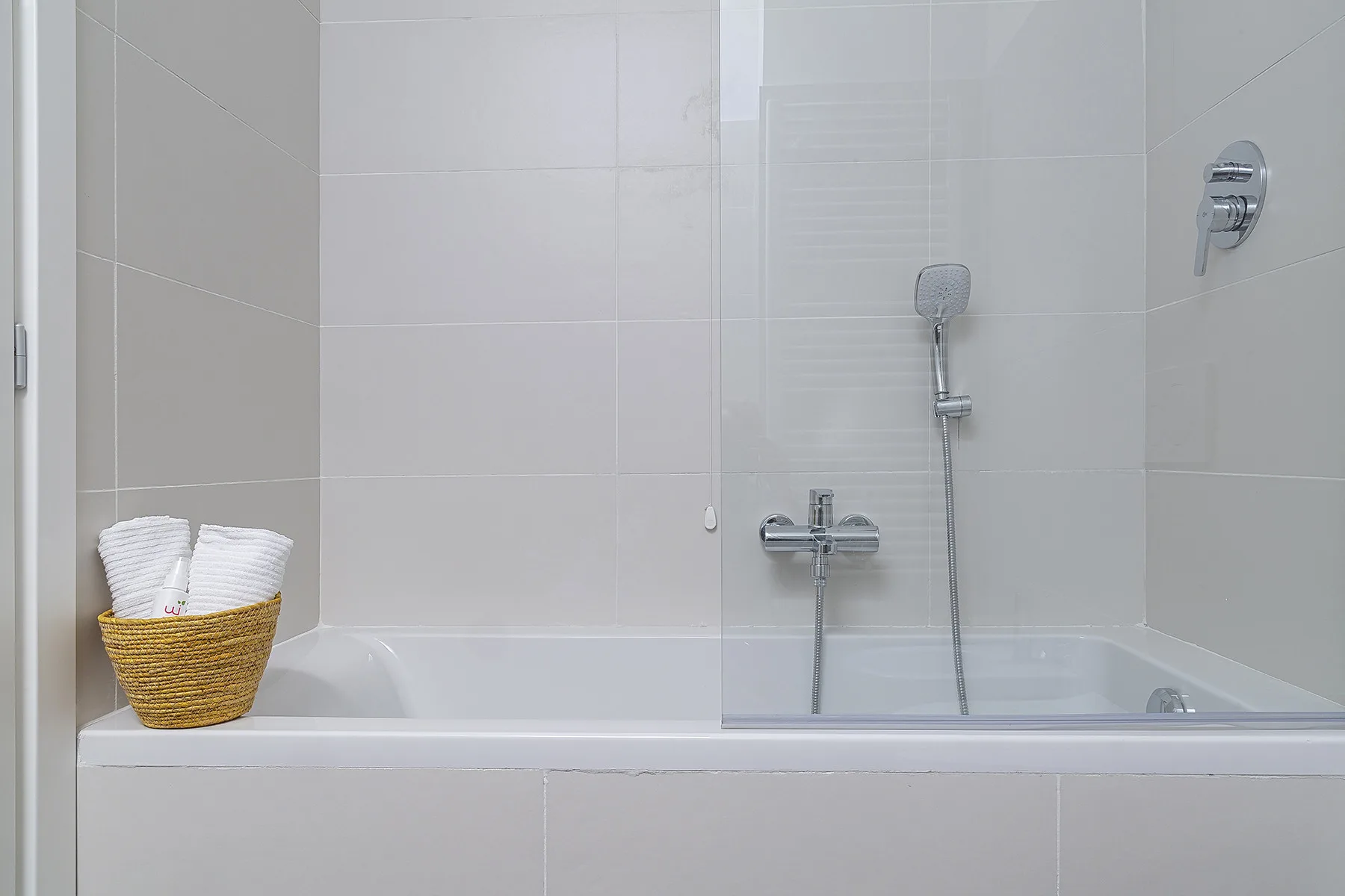 A tiled bathroom with a bathtub, shower fixtures, and folded towels.