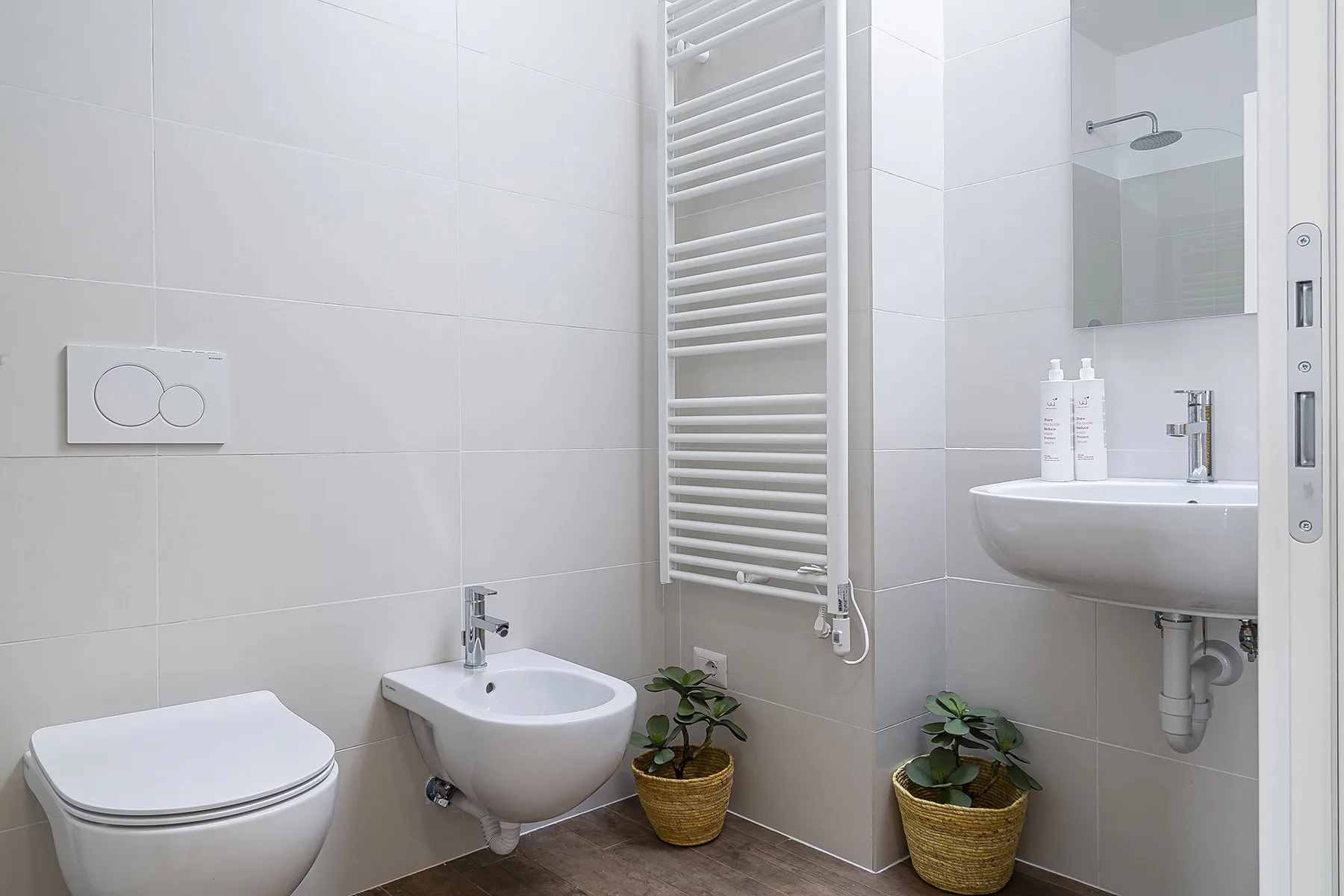 A bright tiled bathroom with a sink, toilet, and wall-mounted towel warmer.