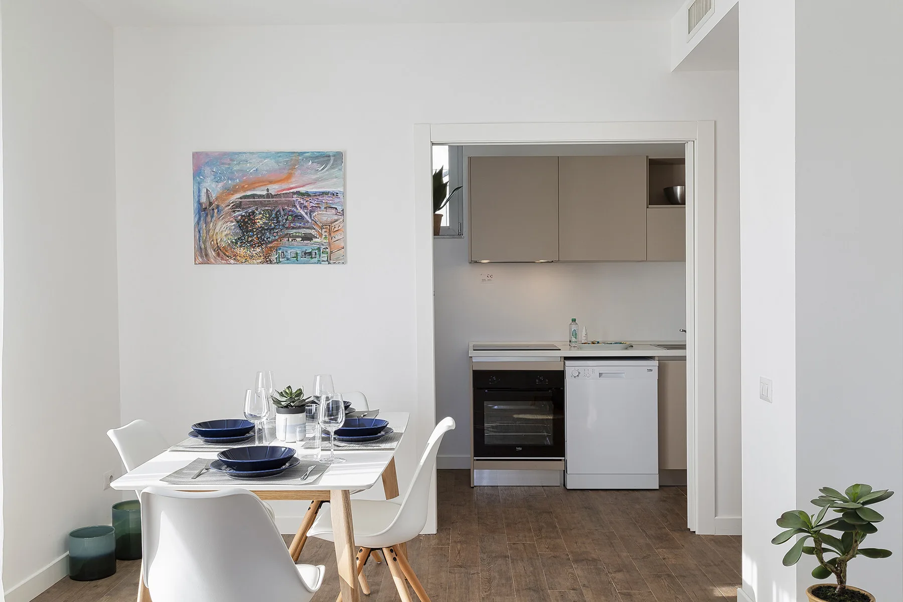 A dining area with a set table opens onto a compact kitchen.