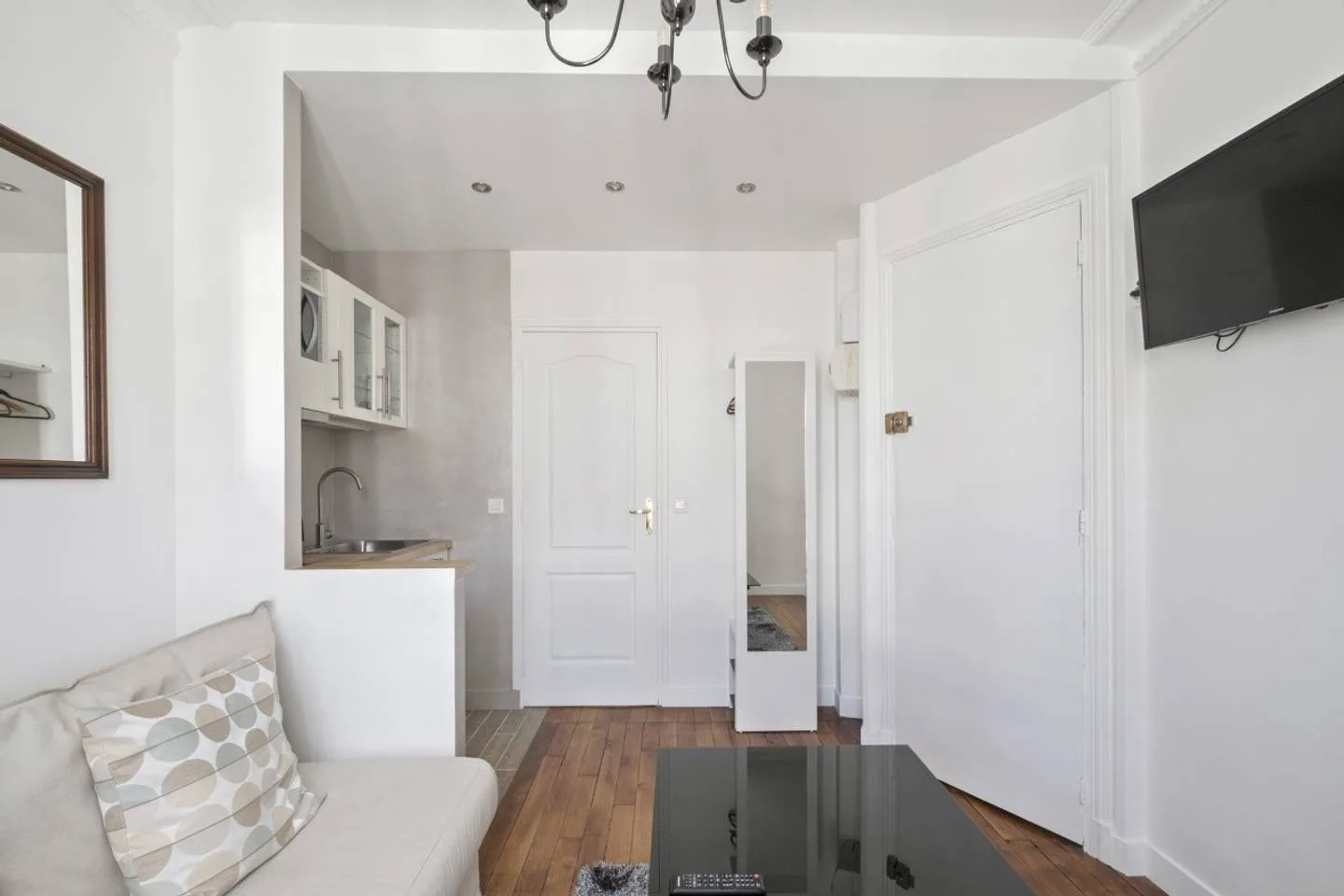 A bright living room with a compact kitchen area and a television.