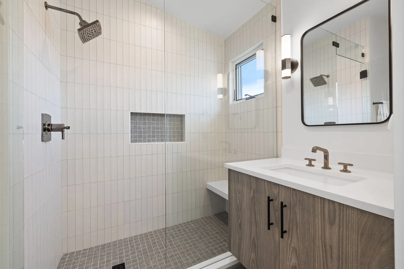 Una ducha con azulejos junto a un lavabo de baño con un espejo grande.